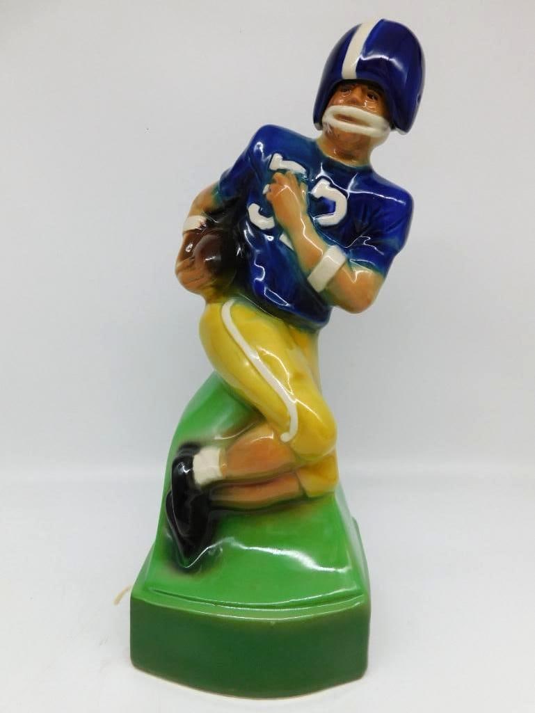 Jim Beam Football Player Decanter Blue Jersey Number 32: A Jim Beam Regal China decanter sculpted as a football player in blue helmet and jersey numbered 32 running hard with the ball tucked under his arm upon a green turf-form base. The sculptor caught a g