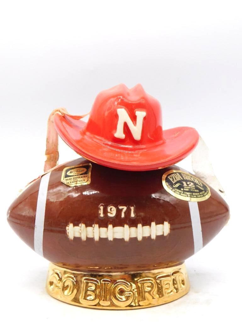 Ezra Brooks Nebraska Cornhuskers Go Big Red 1971 Football Decanter: An Ezra Brooks decanter modeled as a football dated 1971 crowned with a scarlet cowboy hat bearing the Nebraska N and set upon a gold base lettered Go Big Red. Hand decorated in 24 karat gold by