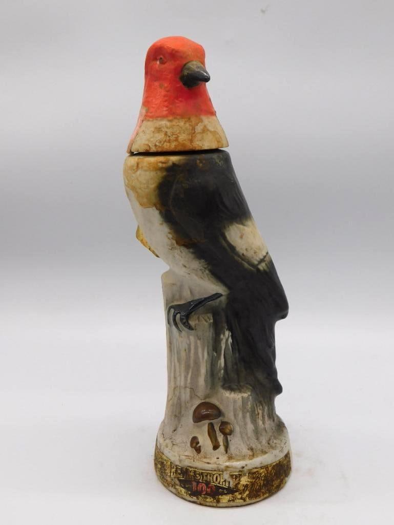 Jim Beam Red-Headed Woodpecker Ceramic Decanter with Hang-Tag: A Jim Beam ceramic decanter modeled as a red-headed woodpecker at rest on a tree stump the plumage brightly painted. A gold hang-tag bearing a poem is still attached. Approximately 12 inches tall.