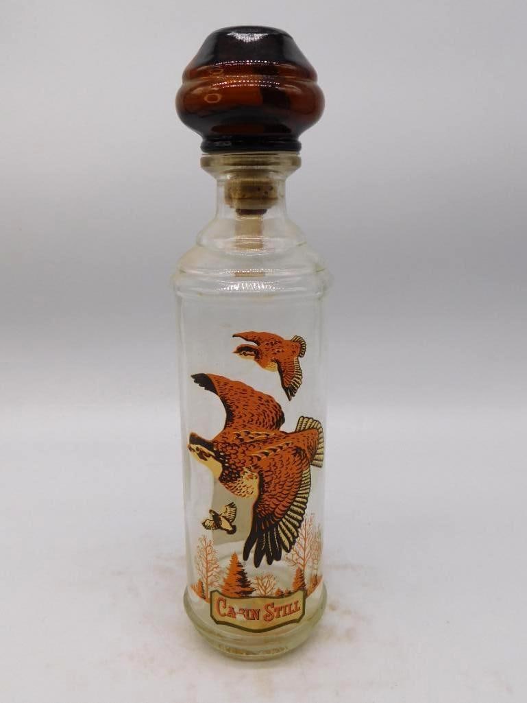Cabin Still Game Birds in Flight Glass Decanter with Amber Stopper: A trim Cabin Still glass decanter the paneled body printed with game birds breaking over a stand of pines in autumn browns and golds. Handsome against a window and the color has held well. Approximate