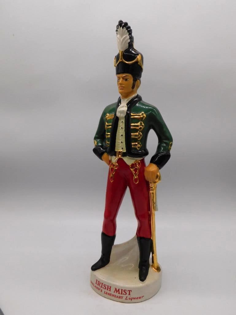 Irish Mist Heublein Soldier Liqueur Decanter 18th Century Irish Character: A ceramic decanter for Irish Mist Ireland's Legendary Liqueur modeled as an 18th-century Irish soldier in a green coat and red trousers with a gold-tone musket at his shoulder. A gallant figure cleanl