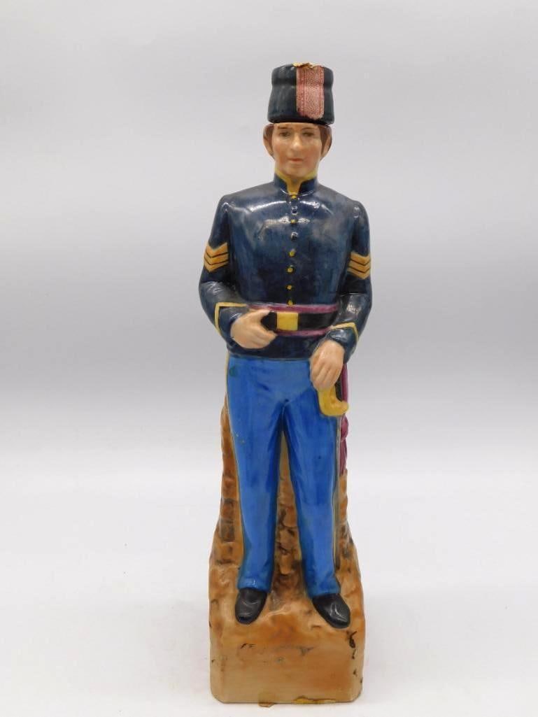Civil War Union Sergeant Ceramic Whiskey Decanter Maker Unmarked: A ceramic whiskey decanter sculpted as a Union Army sergeant in blue dress uniform his gold chevron stripes plainly picked out standing atop a brick-textured pedestal base. Unmarked as to maker. Appro