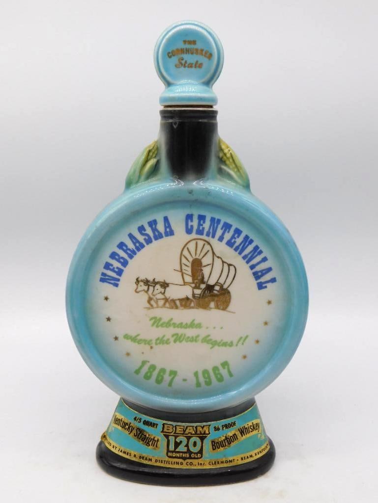 Jim Beam Nebraska Centennial 1867-1967 Cornhusker State Whiskey Decanter: A Jim Beam Regal China decanter struck for the Nebraska Centennial its round face lettered 1867-1967 above a gilt ox team drawing a covered wagon and the motto where the West begins. Ears of corn are 