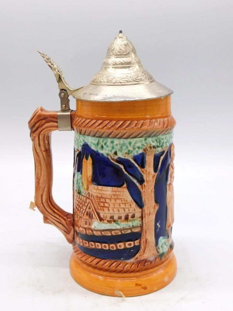 German Style Ceramic Stein Form Whiskey Decanter IV with Pewter Lid: A ceramic stein-form whiskey decanter the fourth of a small group in this collection. A cobalt blue relief village scene runs about the body and a hinged pewter lid crowns it. Stout and well-turned wi