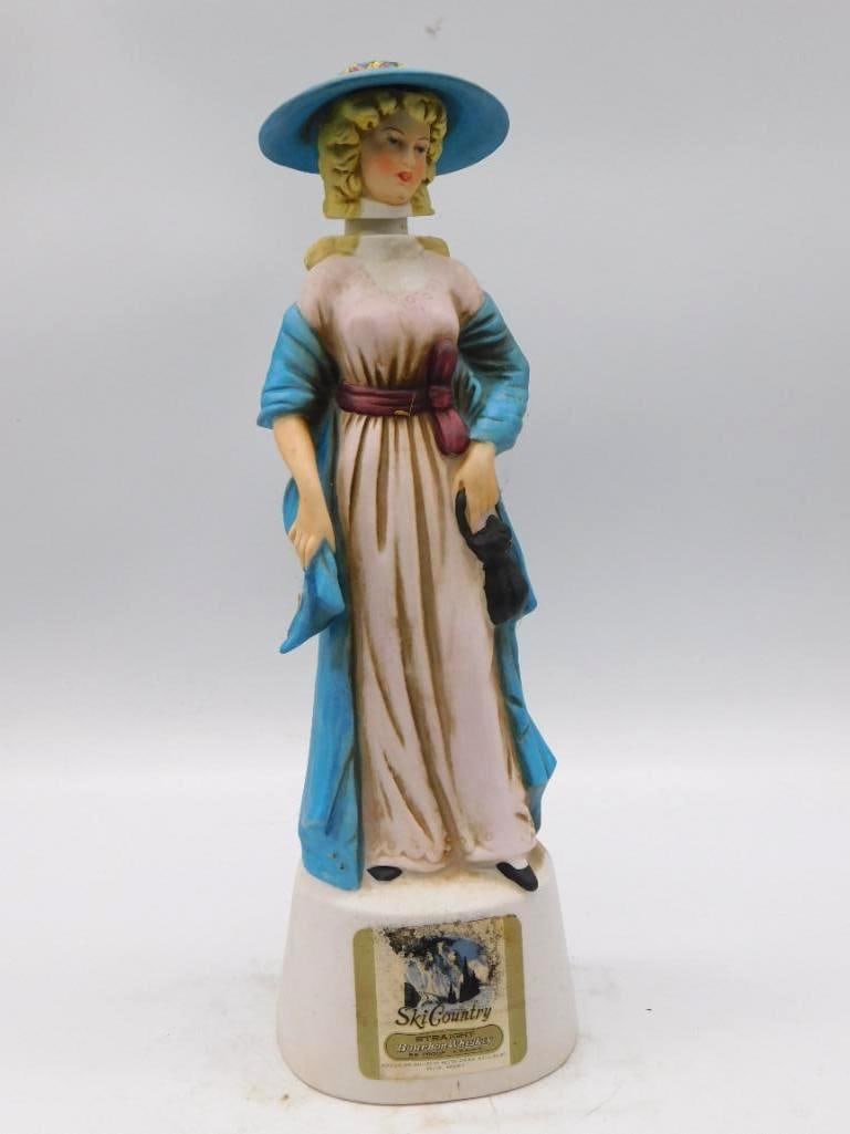 Ski Country Victorian Lady Bourbon Decanter Blue Dress and Plumed Hat: A fetching Ski Country Straight Bourbon Whiskey decanter modeled as a Victorian lady in a light blue dress and plumed hat a small handbag upon her arm. The painter did not stint on the trimming of the
