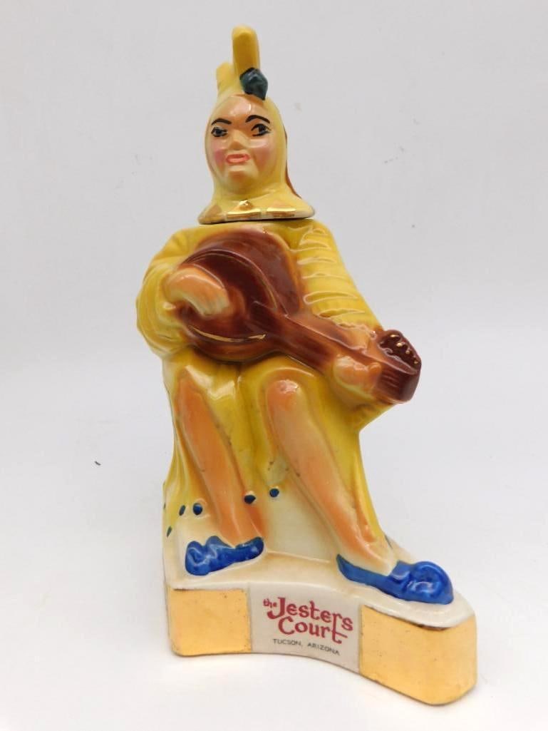 The Jesters Court Tucson Arizona Court Jester Ceramic Decanter: A colorful ceramic decanter sculpted as a court jester in yellow robes lute in hand and a blue slipper turned up at the toe with gilt accents throughout. The base is marked The Jesters Court Tucson