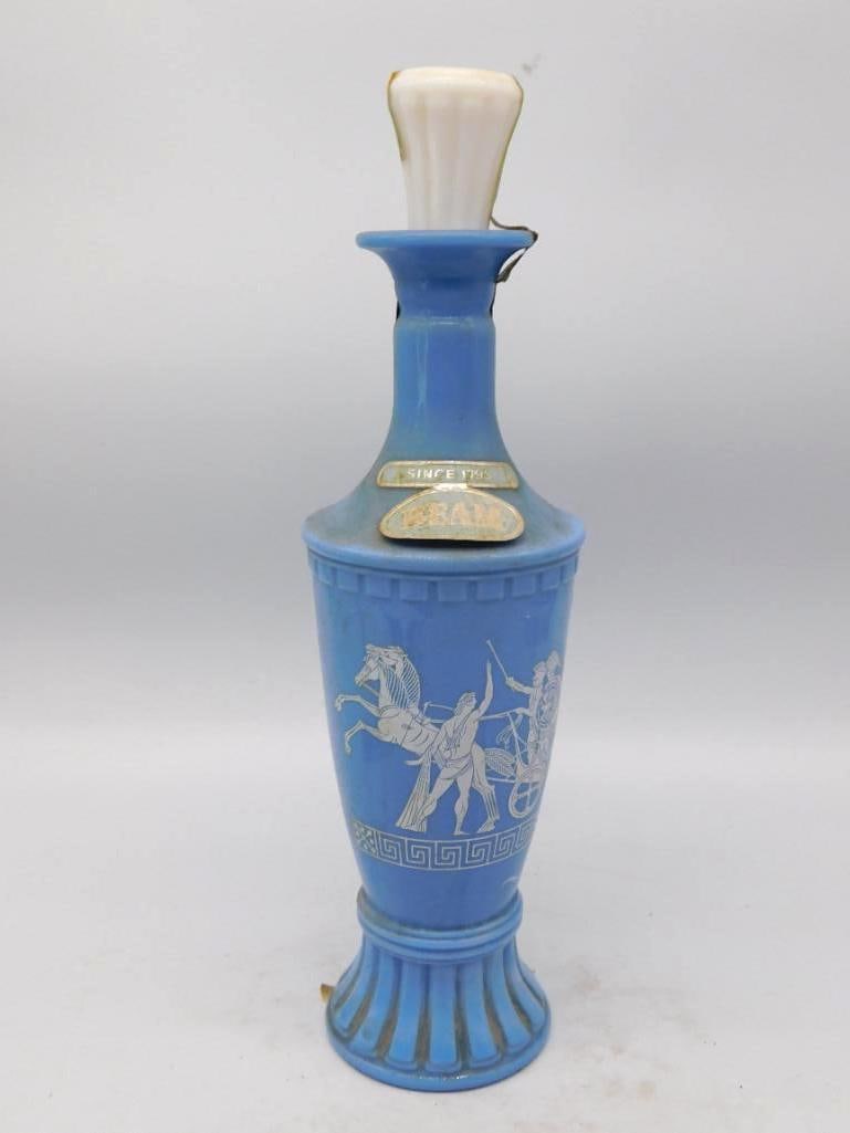 Jim Beam Olympian Light Wedgwood Blue Classical Scene Decanter: A trim Jim Beam Olympian decanter in light Wedgwood blue banded in Greek key and set with white classical warriors driving a chariot. The porcelain stopper is present the gilt neck plaque reads Beam