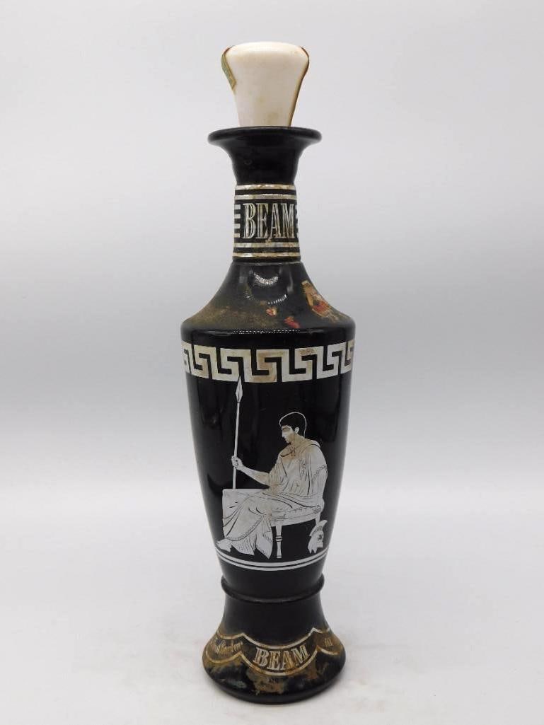 Jim Beam Grecian Black Glass Decanter with Milk Glass Stopper: A trim Jim Beam decanter in black glass banded at the shoulder with a white Greek key and painted with a seated classical figure holding a spear. The milk glass stopper is present and the neck reads