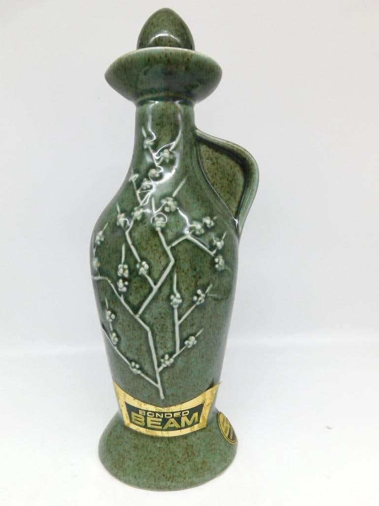 Jim Beam Regal China Green Cherry Blossom Jug Decanter Bonded Beam: A James B. Beam Distilling Co. Regal China decanter in jug form beneath a mottled green glaze its body raised with a white cherry blossom branch and fitted with a side handle. The Bonded Beam gold lab