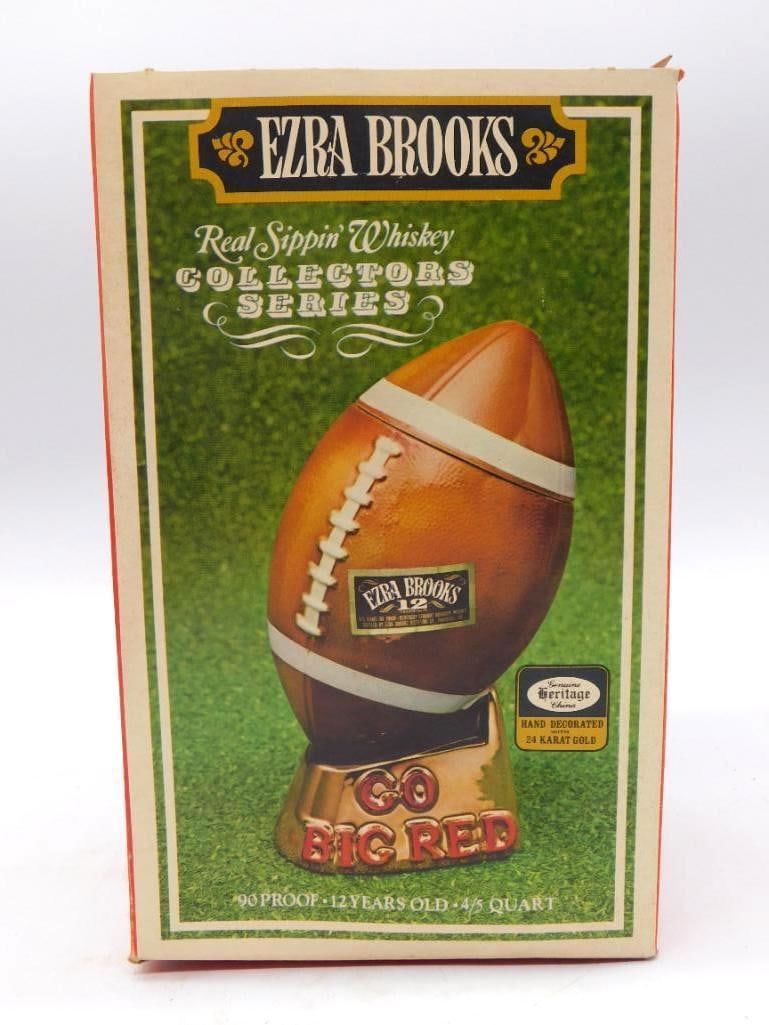Ezra Brooks Nebraska Go Big Red National Champs Football Decanter: An Ezra Brooks ceramic decanter shaped as a football a Nebraska Cornhusker mascot in a red jersey perched atop it. The gold-tone base reads National Champs and Nebraska and the bottle is marked Ezra