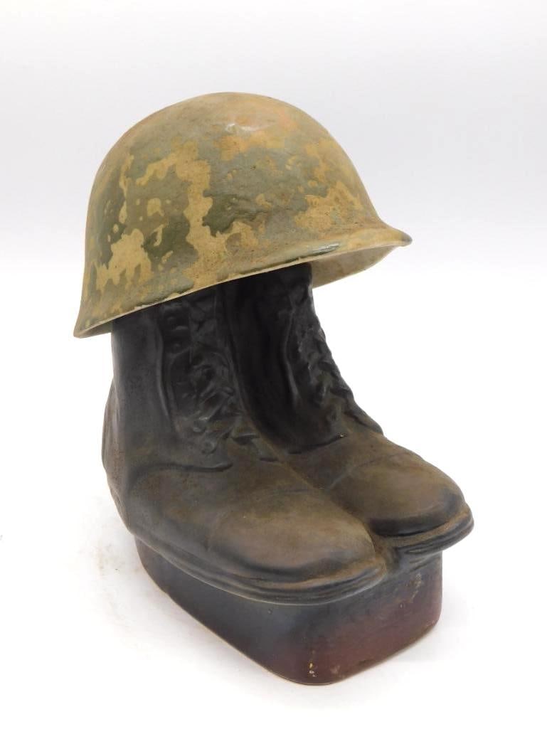 Combat Boots and Helmet Ceramic Military Whiskey Decanter: A ceramic decanter modeled as a pair of lace-up combat boots beneath a camouflage-glazed helmet carrying no maker's brand. A sober and soldierly subject. Measures approximately 10.5 inches as photogra