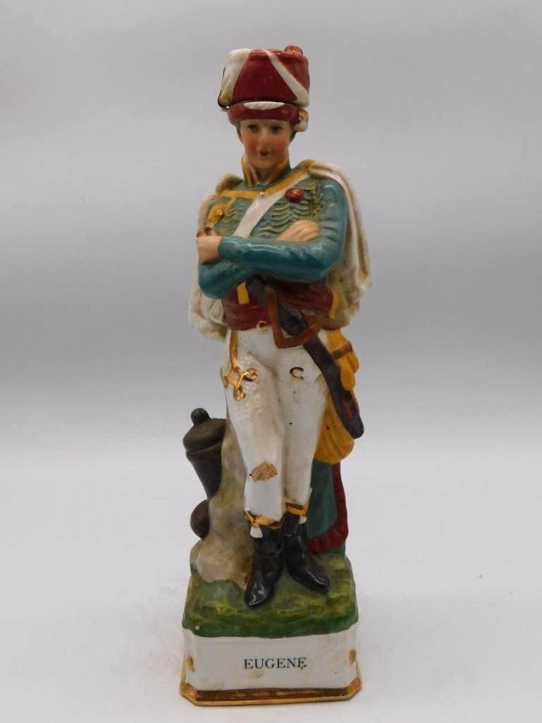 Eugene Napoleonic Officer Ceramic Decanter Teal Uniform: A ceramic decanter modeled as the Napoleonic officer Eugene arms crossed in a teal uniform and white cape a small cannon at his side on a green grass-textured base. A dignified military portrait stand