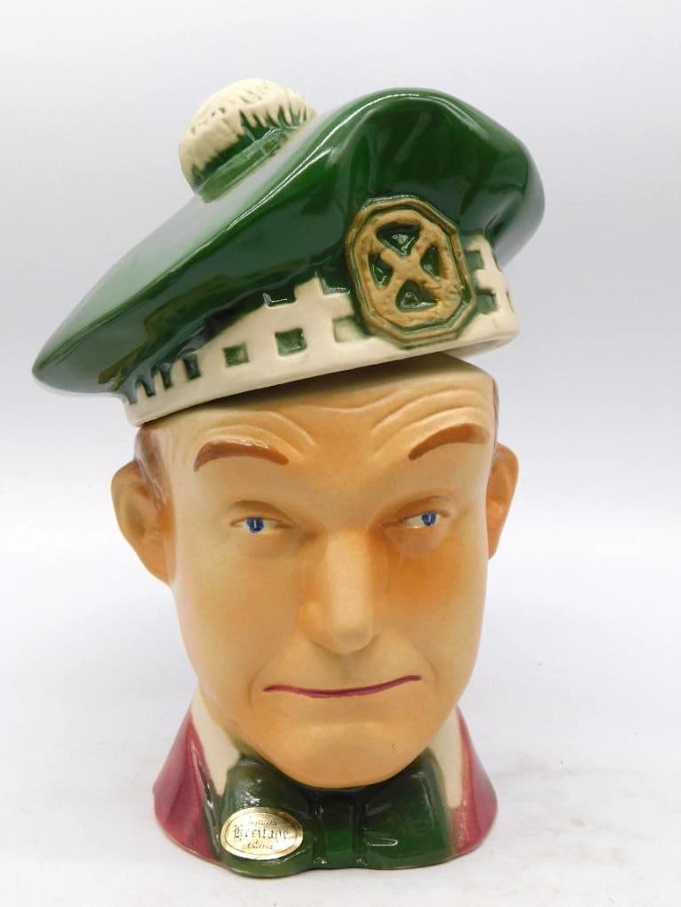 Heritage China Scotsman Head Decanter in Green Tam with Clan Badge: A well-turned head-form decanter modeled as a Scotsman his green tam o'shanter with white toorie and diced band serving as the stopper a clan badge pinned at the side. The face is capably painted blue