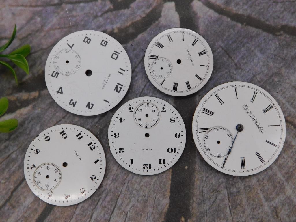 Watch Parts: Case Rings, Dials, and Timing Gauge Lot: Watchmaker's parts box containing several aluminum watch case sizing rings, two enamel pocket watch dials, and a metal case sizing gauge with a printed measurement grid. A ruler photo shows the box is