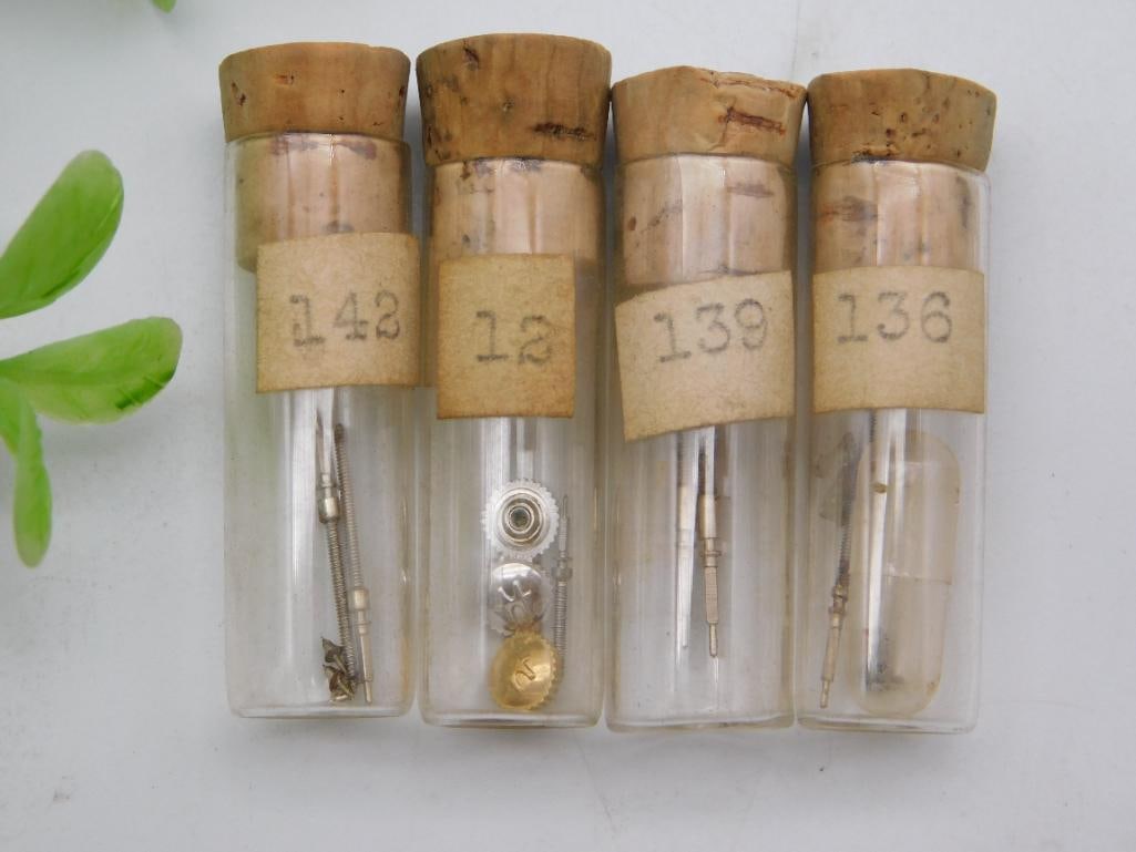 Watch Stem & Gear Parts Vials, Lot of 4: Four numbered corked vials (142, 12, 139, 136) containing watch winding stems along with a small fluted crown, a gear, and a brass component. See photos for exact size and condition.
