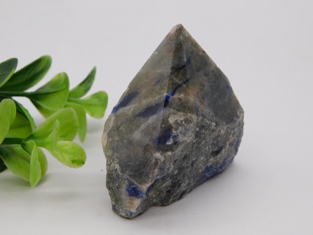 Mineral - Sodalite Rough Specimen with Pyrite Inclusions: Rough natural mineral specimen in gray-blue tones with visible sodalite blue veining and scattered gold pyrite flecks, showing a partially crystallized pointed face. Lot label reads "714007, 2026