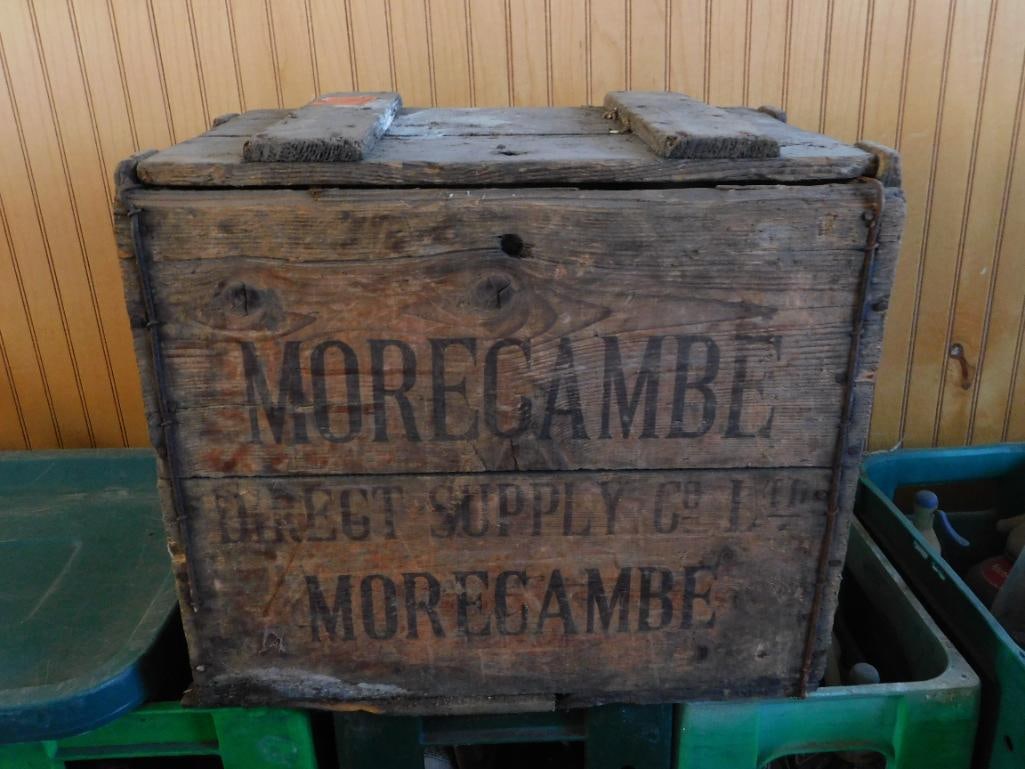 Antique Morecambe Wood Crate with 6 Glass Soda Syphons: This lot features a weathered wooden advertising crate stenciled 'MORECAMBE / DIRECT SUPPLY CO. LTD. / MORECAMBE,' holding six vintage glass soda syphon (seltzer) bottles with red and blue lever spray
