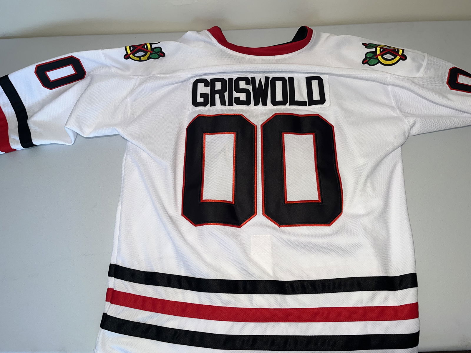 Clark Griswold Chicago Blackhawks Movie Replica Jersey Size XL: This is a white replica Chicago Blackhawks hockey jersey, modeled after the iconic garment worn by the character Clark Griswold, portrayed by Chevy Chase, in the 1989 holiday film National Lampoon's
