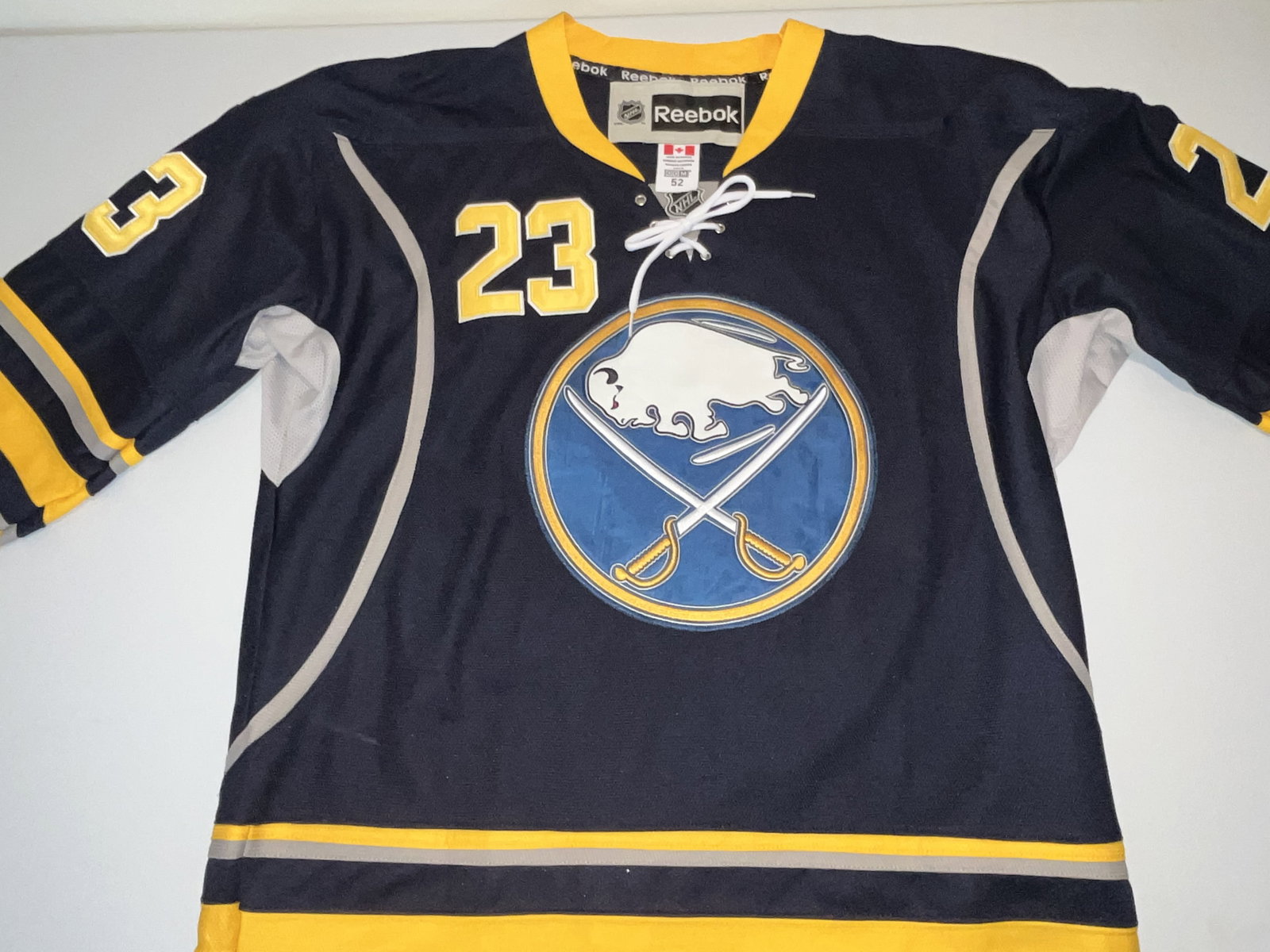 Sam Reinhart Buffalo Sabres Reebok Authentic On-Ice Style Jersey, Size 52: This is an authentic Buffalo Sabres home jersey manufactured by Reebok, styled for forward Sam Reinhart. The jersey features the team's classic navy blue, gold, and white colorway. It is constructed w
