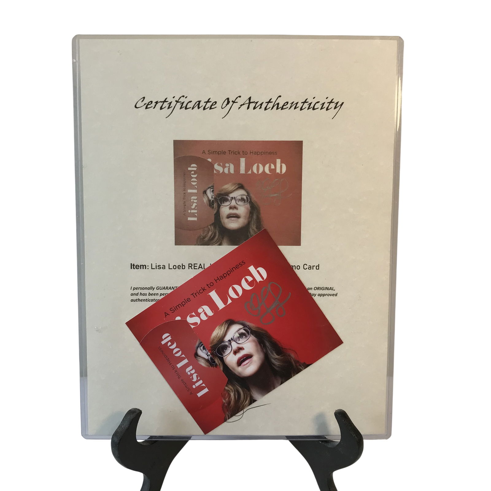 Lisa Loeb Autographed A Simple Trick to Happiness Promotional Card and Certificate of Authenticity: This lot consists of a promotional card for the Lisa Loeb album A Simple Trick to Happiness. The square card features a photographic portrait of Loeb and includes printed text for the album title and