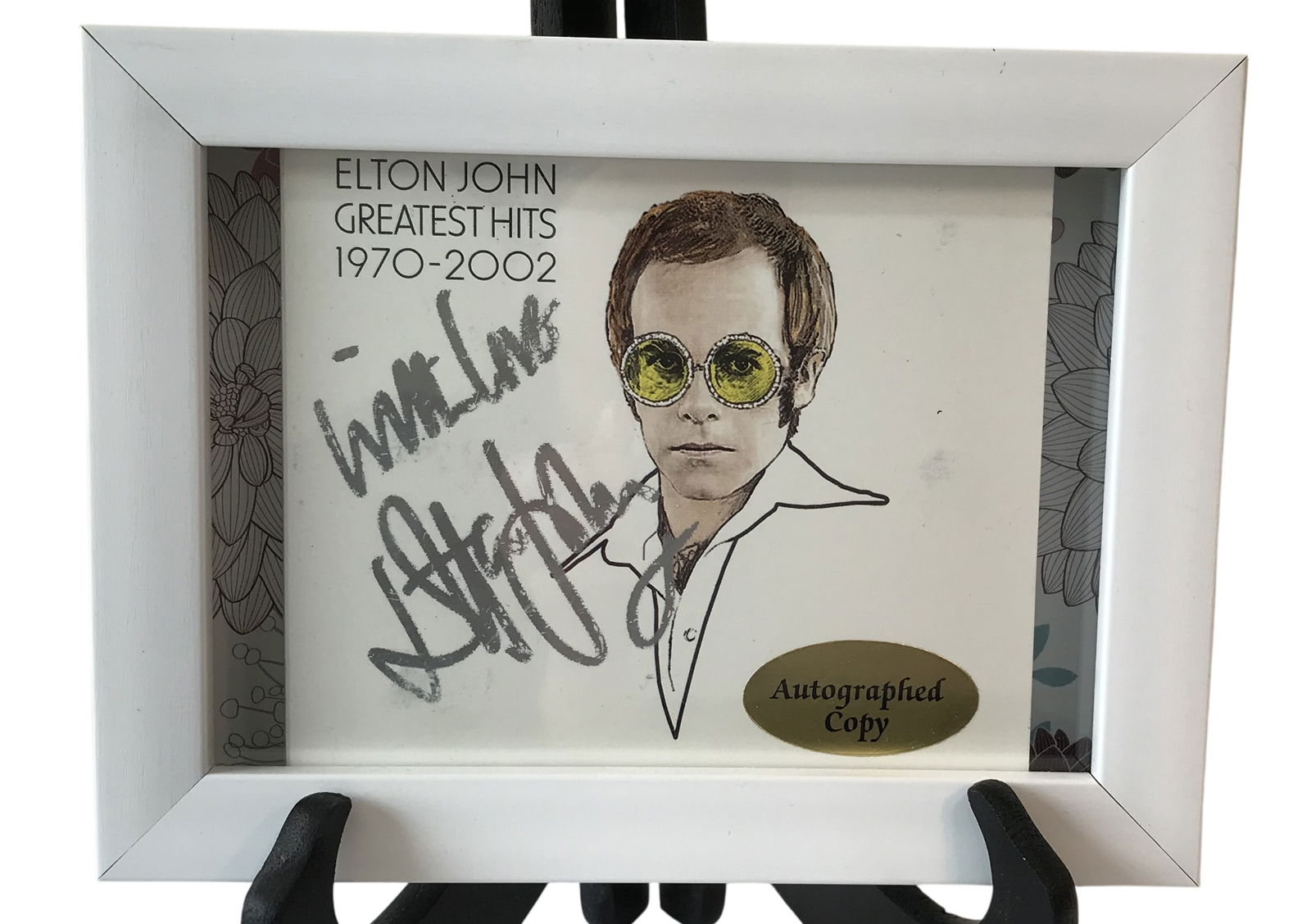 Elton John Autographed Greatest Hits 1970-2002 Framed Print: This framed print features artwork associated with the Elton John Greatest Hits 1970-2002 collection, depicting a stylized line drawing of the artist wearing yellow-tinted glasses.