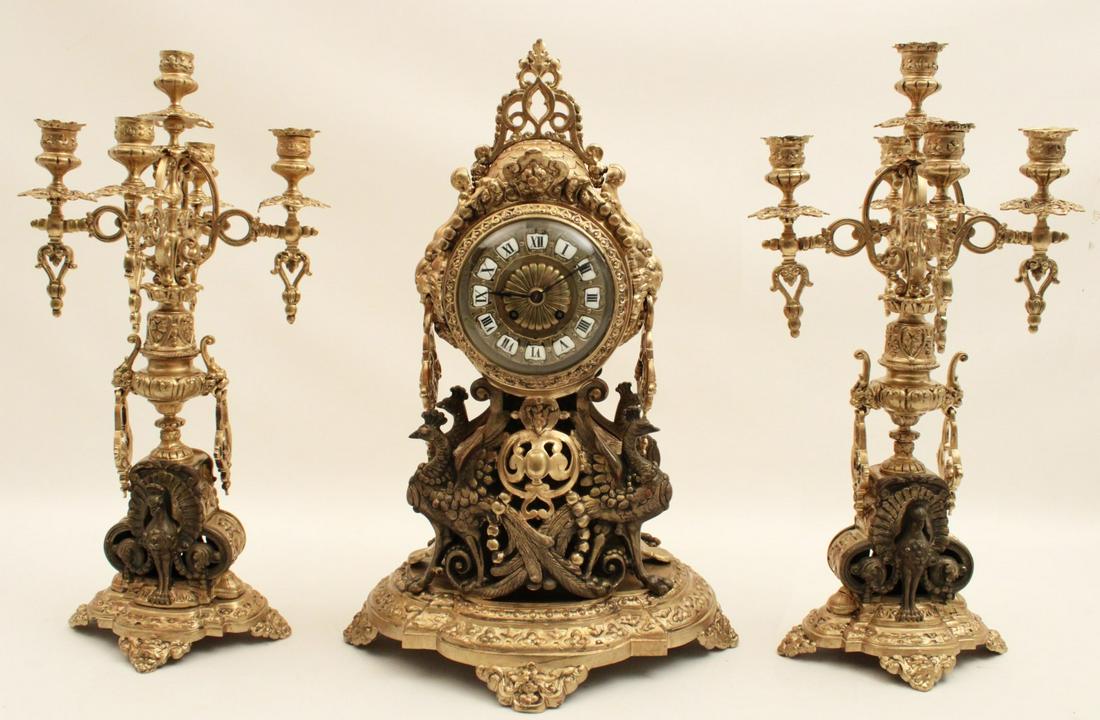 UNUSUAL 3 PC. FRENCH GILT BRONZE CLOCK SET: UNUSUAL 3 PIECE FRENCH GILT BRONZE CLOCK SET HAVING RAISED ENAMEL NUMERAL DIAL AND LION HEAD HANDLES, SUPPORTED BY PARTIAL GILT PEACOCKS, 19TH C.; 21"H X 13.5"W X 8"D