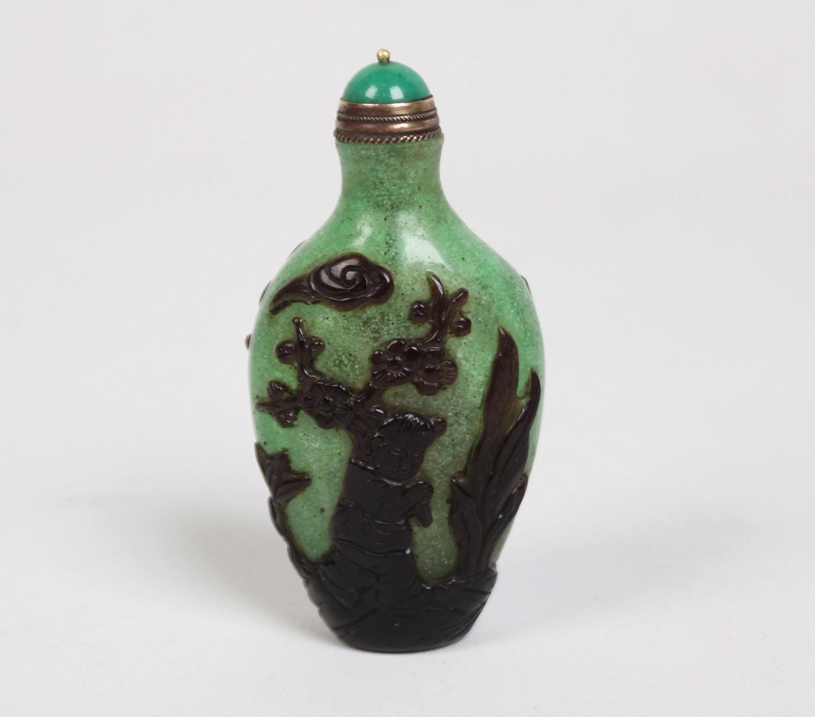 RARE GREEN SNOWFLAKE PEKING GLASS SNUFF BOTTLE: RARE GREEN SNOWFLAKE PEKING GLASS SNUFF BOTTLE WITH SINGLE GLASS OVERLAY IN FLATTENED OVAL SHAPE SITTING ON A ROUND RAISED FOOT, SINGLE GLASS OVERLAY IS CARVED OF MAN ON HORSEBACK WITH BAT DESCENDING 