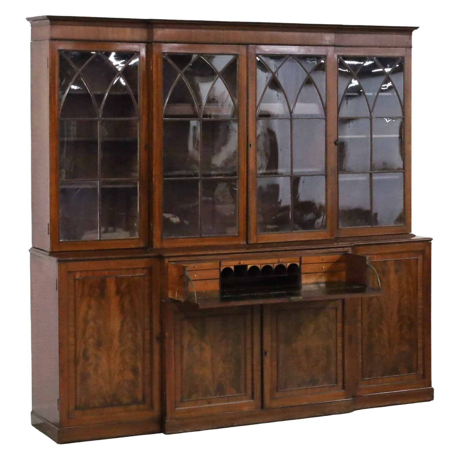 ENGLISH MAHOGANY BREAKFRONT BOOKCASE, 19TH C.: Stately English mahogany breakfront bookcase, the upper cabinet with pointed arch mullion doors maintaining their original glass, the lower cabinet with fitted secretaire drawer, side cabinets also fi