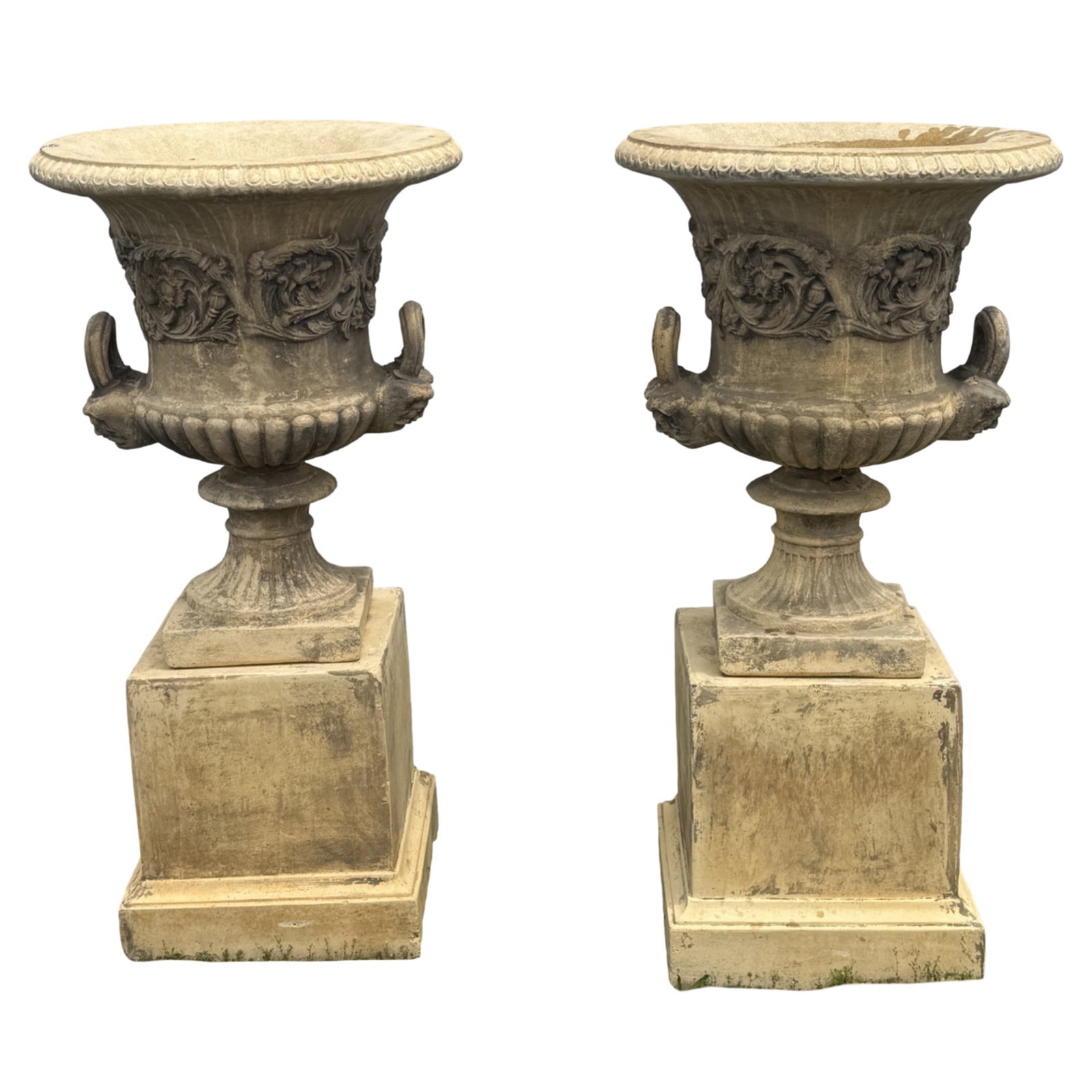 PR CLASSICAL CAST STONE GARDEN URNS ON PLINTHS: Large pair of classical cast stone double handled garden urns, waisted body, scrolling foliate relief motif, a gadrooned basin, and an egg and dart rim, resting on seperate stone plinths, 20th century