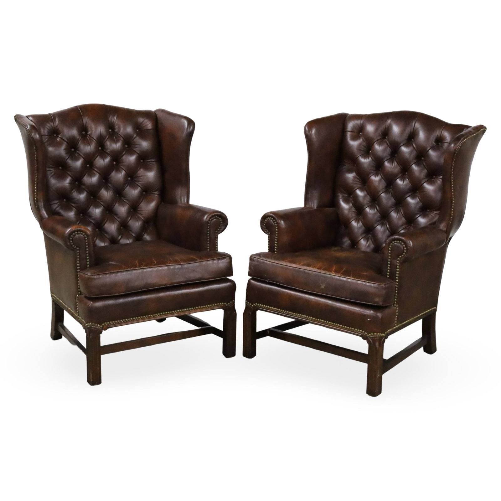 PR TUFTED LEATHER WINGBACK ARMCHAIRS: Pair of Georigan style tufted brown leather wingback armchairs with brass nailhead trim, raised on straight fluted legs, 20th century; 43"H 28"W 26"D