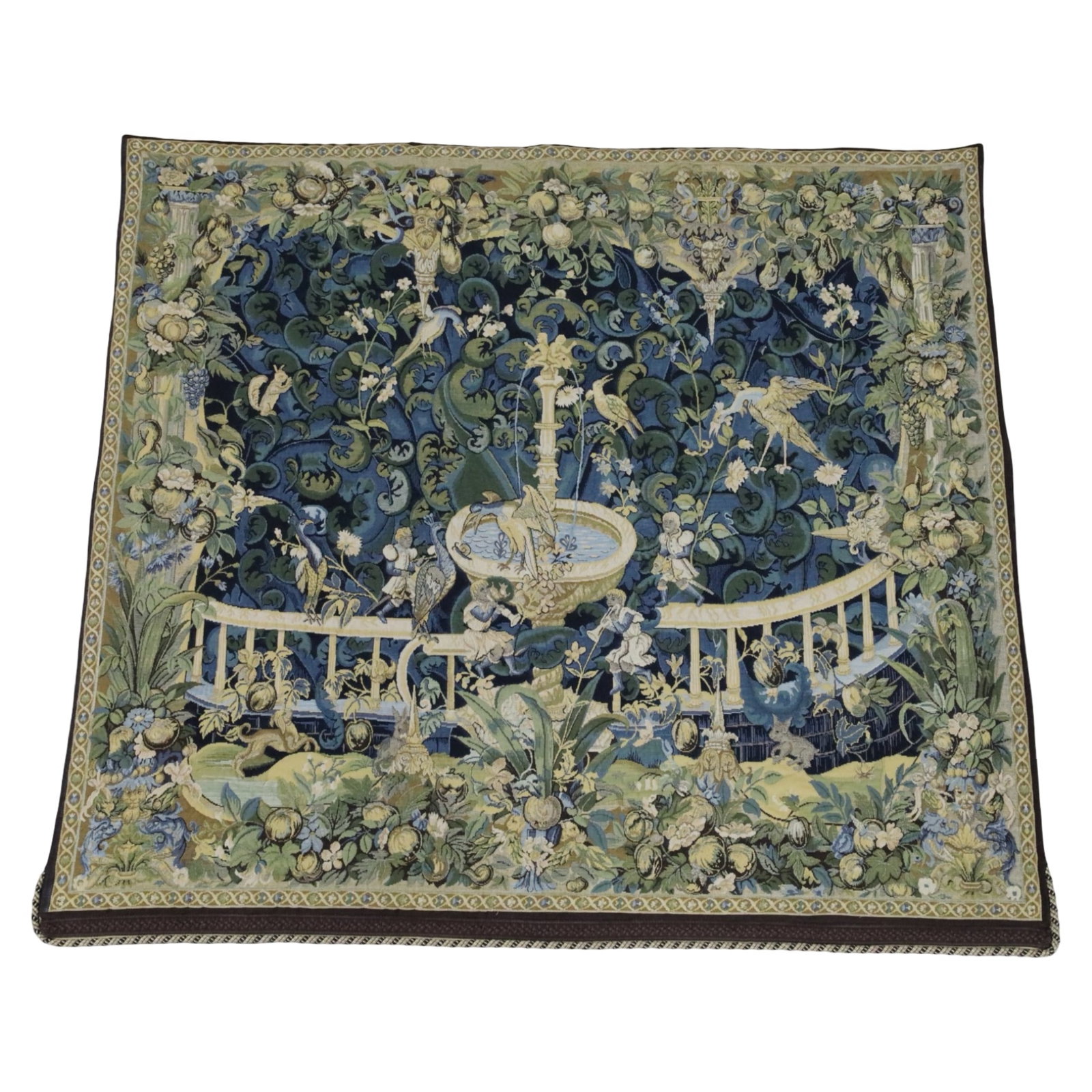 FLEMISH BAROQUE STYLE VERDURE TAPESTRY: Flemish Baroque style verdure tapestry, depicting exotic birds, animals, and musicans gathering around a fountain in a highly foliated landscape, after the 14th century tapestry seen in the Vienna