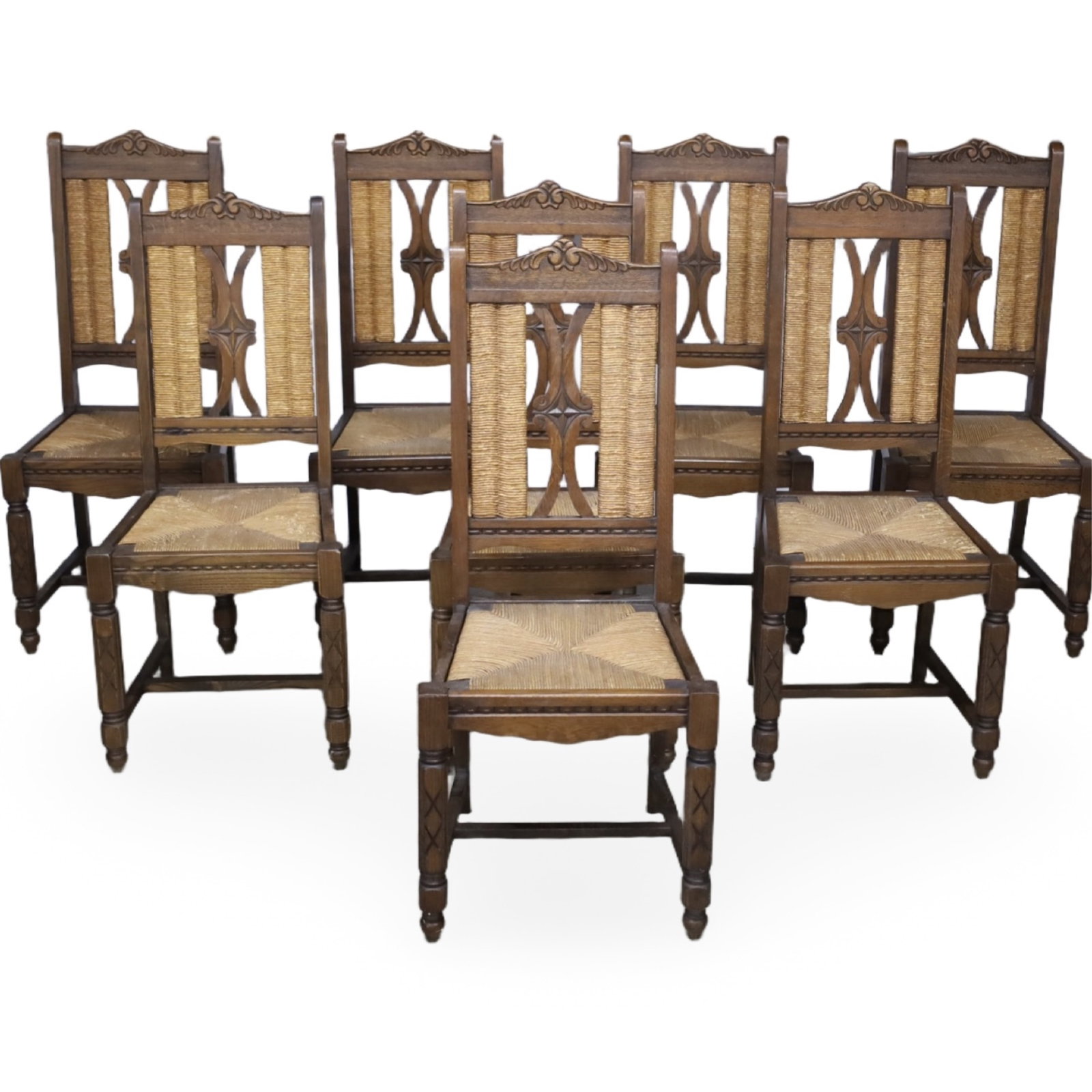 SET OF EIGHT HENRI II STYLE OAK DINING CHAIRS: Set of eight French carved oak dining chairs with pierced backs and rush seats, offered as one lot. Measures 18.5"W x 15.5"D x 42"H.
