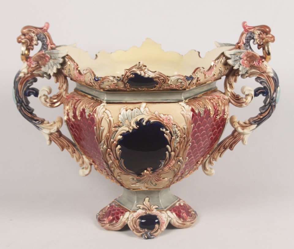 LARGE FAIENCE STYLE PORCELAIN FOOTED JARDINIERE: LARGE FAIENCE STYLE PORCELAIN FOOTED JARDINIERE HAVING WINGED GRIFFIN SURMOUNTED DOUBLE HANDLES, IMPRESSED MARK ON REVERSE "MADE IN AUSTRIA 1163"; 21"H X 28"W X 18"D; CONDITION: DAMAGE TO ONE QUADRANT