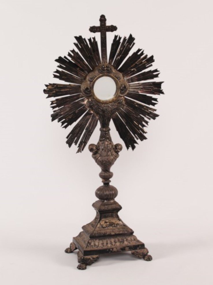 SILVER EMBOSSED MONSTRANCE: SILVER EMBOSSED MONSTRANCE WITH CUPID IN RELIEF ON PAW FEET; 25.5"H X 12.5"W; CONDITION: SILVERSMITH TOUCH MARKS ALONG FRIEZE OF BASE, OXIDATION AND DISCOLORATION TO METAL THROUGHOUT