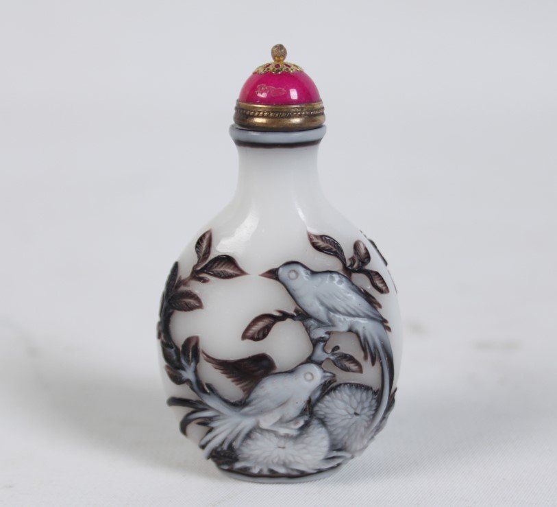 WHITE MILK GLASS PEKING SNUFF BOTTLE: WHITE MILK GLASS PEKING SNUFF BOTTLE IN FLATTENED ROUND SHAPE WITH TWO GLASS OVERLAYS OF BROWN AND WHITE, SITTING ON A RAISED OVAL FOOT WITH A FLARED NECK AND FLAT MOUTH, BROWN AND WHITE CARVING ON FR