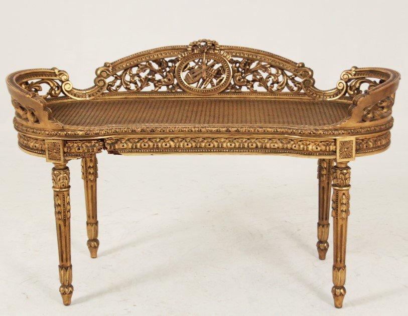 LOUIS XVI STYLE GILT WOOD KIDNEY SHAPED BENCH: LOUIS XVI STYLE GILT WOOD KIDNEY SHAPED BENCH HAVING OPEN WORK INSTRUMENT CARVED BACK DESIGN AND CANE BOTTOM, LATE 19TH/20TH C.; 27"H X 42"W X 16"D