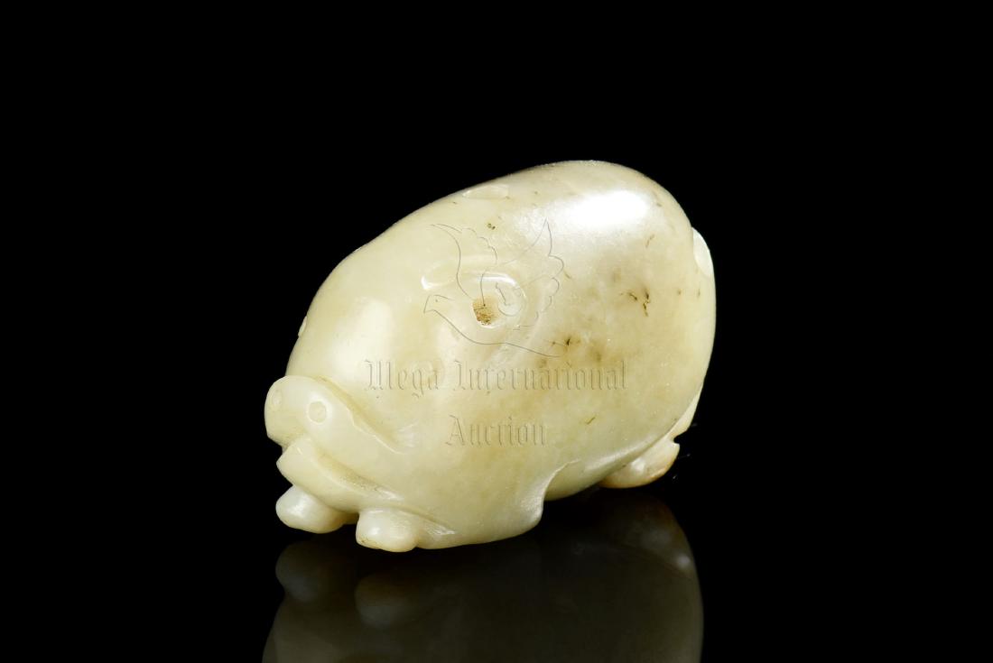 HETIAN JADE CARVED 'PIG' ORNAMENT: The Hetian jade carved ornament depicts a pig lying recumbent on the ground, ears laid back with eyes open, the jade is of yellowish-celadon color tone with russet and translucency. Height: 3/4 in (1.