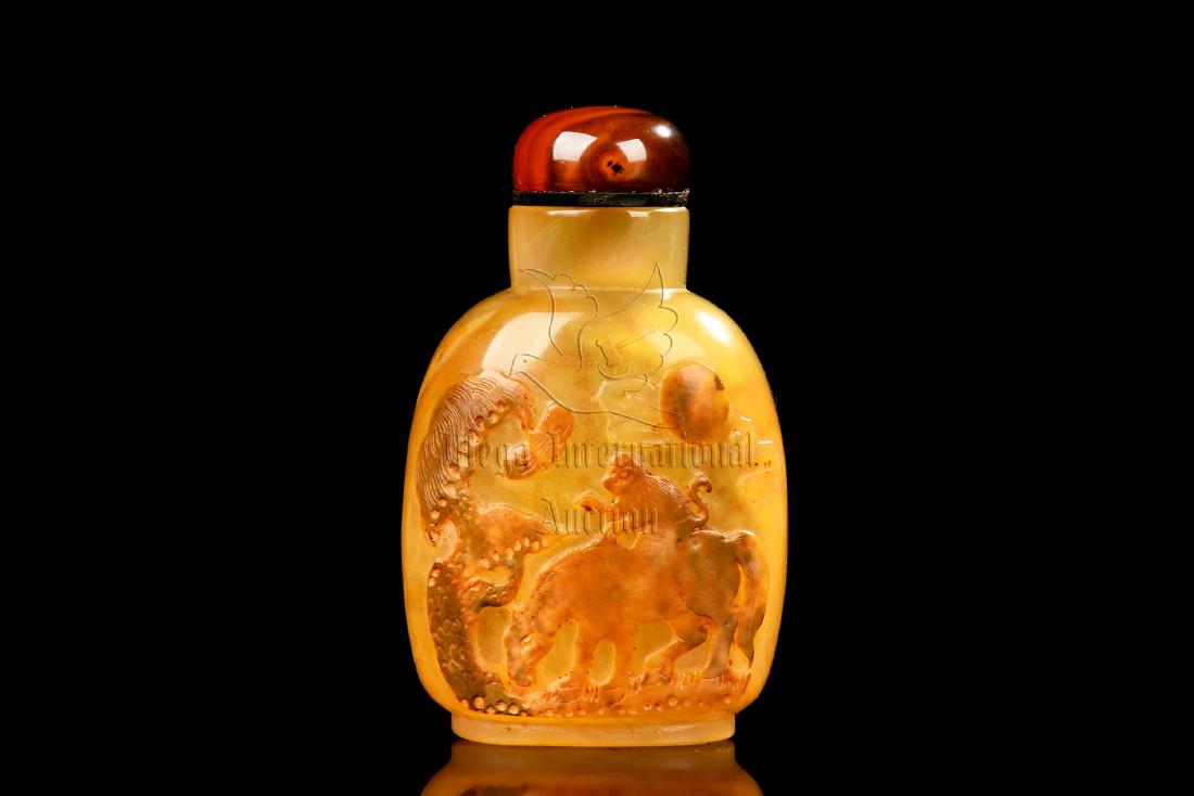 AGATE CARVED 'MONKEY' SNUFF BOTTLE: The agate snuff bottle is of flattened ovoid form, the surface cleverly carved with a monkey riding on the horseback near pine trees, the agate is of yellowish color tone with translucency, complete w