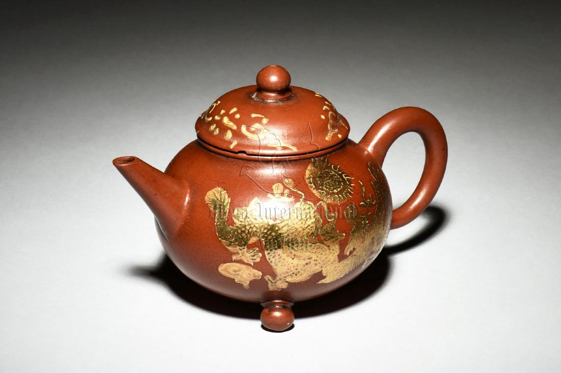 YIXING ZISHA PARCEL GILT TEAPOT: The Yixing Zisha teapot is of globular form, stands on three bead feet, body parcel gilt with dragons and flowers, the clay is of reddish-orange color tone, marks beneath the lid and on the bottom. He