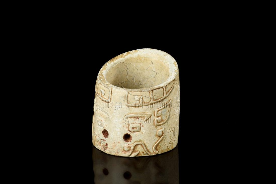 JADE CARVED TAOTIE MASK THUMB RING: The jade thumb ring carved on the exterior with a taotie mask along with archaic scrolling patterns, the jade is of chicken-bone like yellowish-white color tone with russet. Western Zhou Dynasty perio
