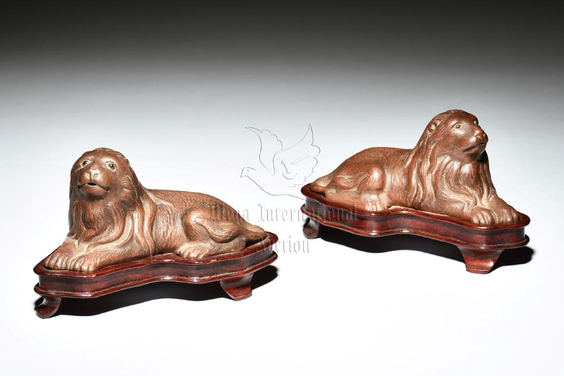 PAIR OF YIXING ZISHA DOG FIGURES WITH STANDS: The lot includes a pair of Yixing Zisha dogs, each rests on en-suite wood carved stand, with head raised and long manes flowing down from the sides, the clay is of brown color tone. Height: 2 in (5.1 