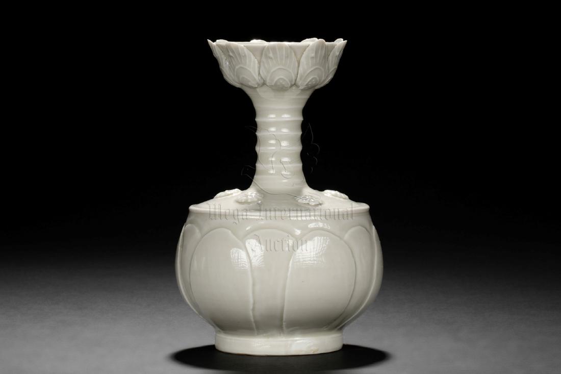 WHITE GLAZED FLORIFORM VASE: The body is of globular form with flower petal design, the shoulder decorated with flowers, the slender neck with ring shapes, leading to flower petal designed rim, glazed overall in white. Height: 5 