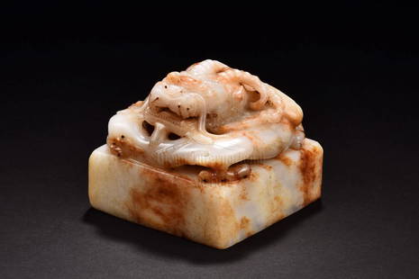 WHITE JADE CARVED 'DRAGON' STAMP SEAL: Carved from white jade, the square seal stamp mounted with a dragon on the top, carved in relief, body curled under its large open mouth, the bottom carved with four character mark. The jade is of