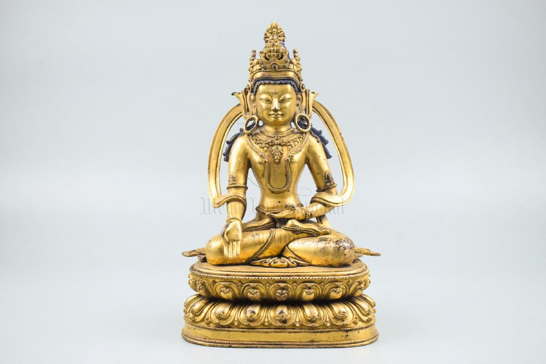 GILT BRONZE AVALOKITESHVARA SEATED FIGURE: The gilt bronze figure depicts Avalokiteshvara seated in dhyanasana on double lotus throne, two at waist level in mudra, wearing ornate robe, headdress, and decorations, bottom bears vajra mark. Heigh