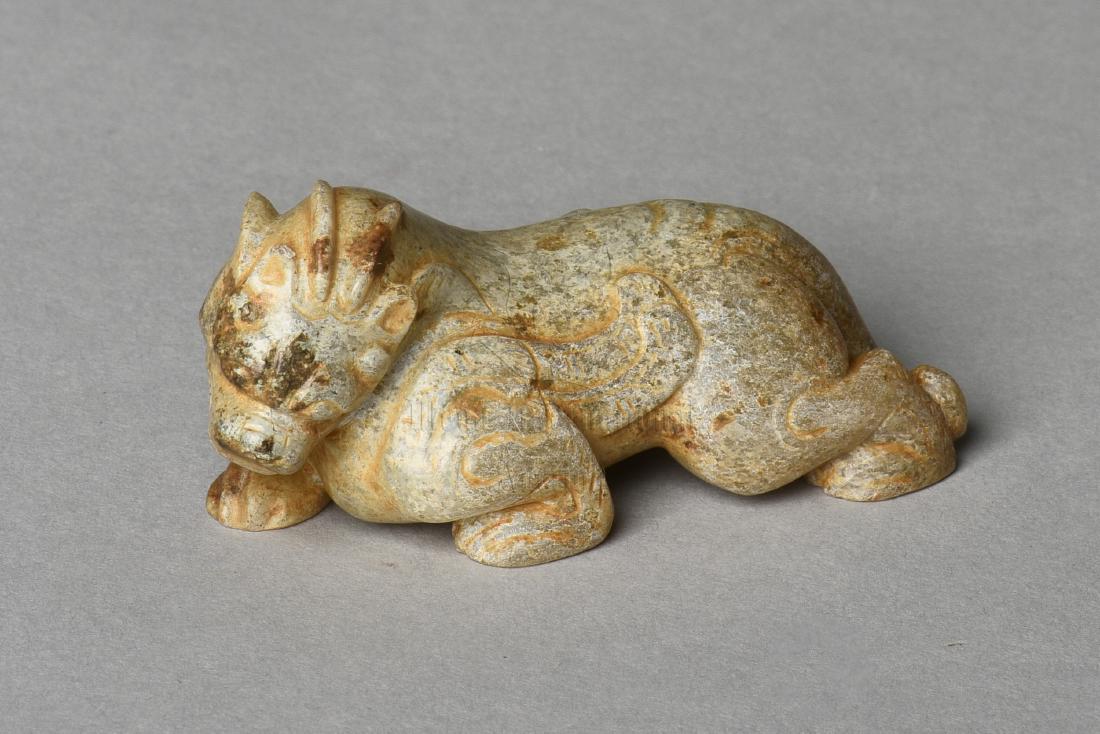 ARCHAIC JADE CARVED 'MYTHICAL BEAST' FIGURE: The archaic jade figure carved in the form of a mythical beast prowling forward, with wings closed and head looking downwards, the jade is of chicken-bone white color tone with russet. Han Dynasty per