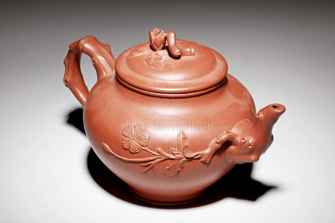 YIXING ZISHA 'PLUM FLOWERS' TEAPOT: The Yixing Zisha stoneware teapot is of bulbous form, the body depicts plum flowers and branches, with branch shaped spout, handle, and finial, the clay is of brown color tone, and the teapot has a to