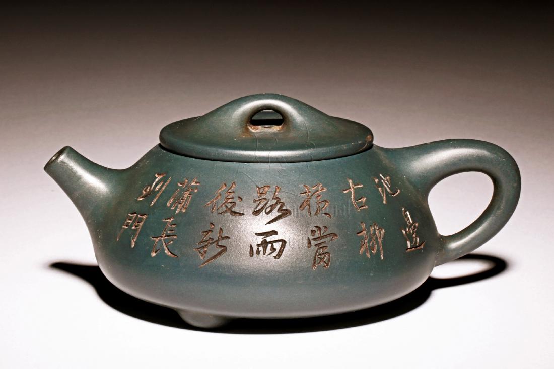 YIXING ZISHA 'POETRY CALLIGRAPHY' TRIPOD TEAPOT: The Yixing Zisha stoneware teapot is of expanded form, the body stands on three short feet, incised on both sides with poetry calligraphy, the clay is of dark green color tone, and the teapot has a to