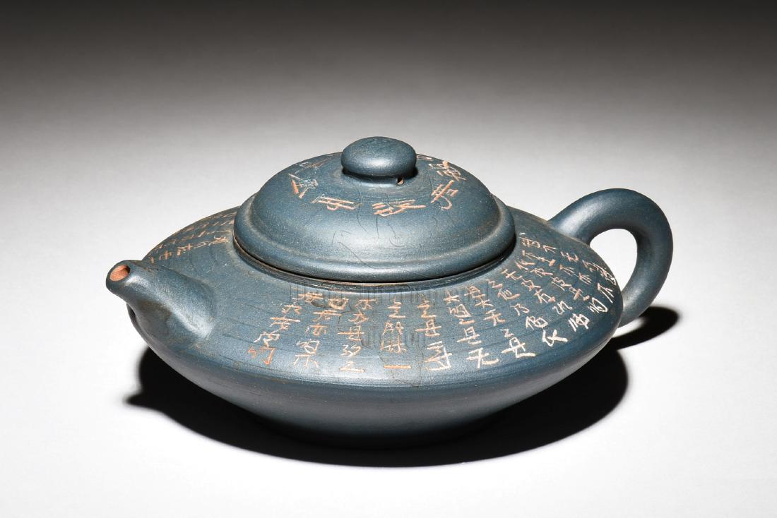 YIXING ZISHA 'POETRY CALLIGRAPHY' TEAPOT: The Yixing Zisha stoneware teapot is of compressed form, the body sharply tapers off at the center, with the top inscribed with poetry calligraphy, the clay is of dark blue color tone, and the teapot