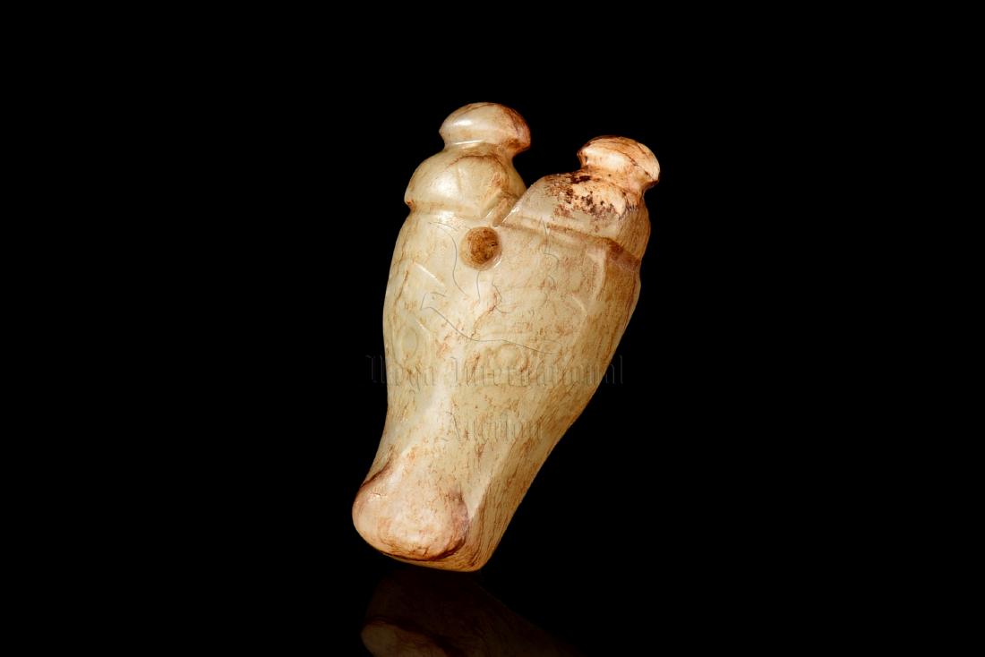 JADE CARVED 'BEAST MASK' ORNAMENT: The jade ornament carved in the form of a beast mask, with detailed eyes, nose, horns, and mouth, the jade is of celadon-white color tone with russet. Western Zhou Dynasty period. Length: 1 3/4 in (4.