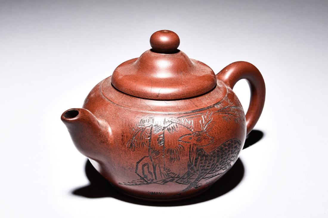 A CHINESE YIXING ZISHA TEAPOT: Of bulbous form with straw-hat shaped lid, the teapot's body depicts a deer in forest scene, mark on the bottom. Height: 3 in (7.6 cm) Width: 5 in (12.7 cm) 宜興紫砂壺